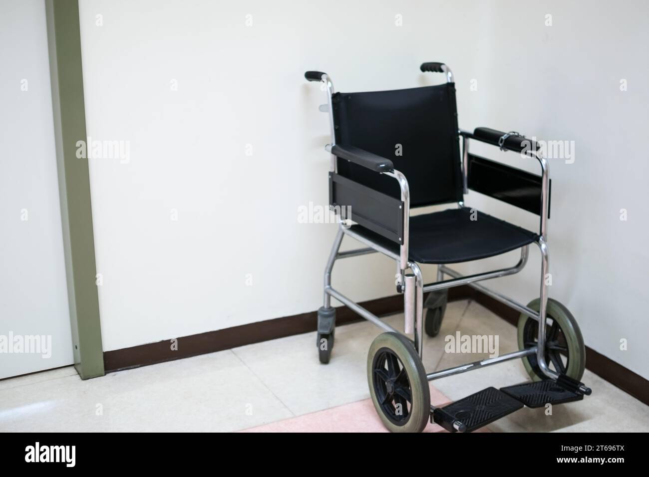 Fauteuil roulant noir sur le sol de l'hôpital avec fond blanc Banque D'Images