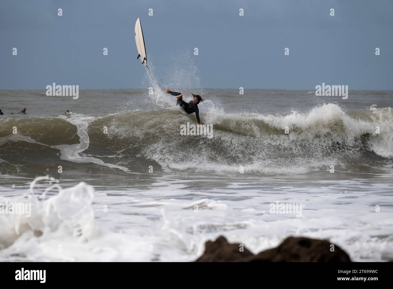 Surfeur lance la planche sur la vague. Une laisse attachée à l'arrière de la section de queue de la planche, empêche de la perdre aux rochers qui se profilent au premier plan. Banque D'Images