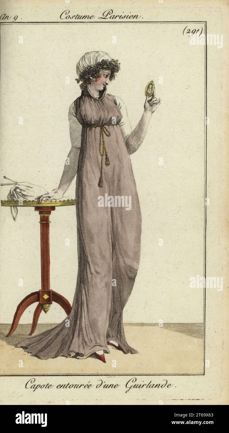 Femme à la mode regardant un portrait miniature dans un médaillon, 1801. Elle porte une capuche capote ornée d'une guirlande, une longue robe à col haut avec cordon sous le buste. Un sac à aiguilles repose sur une table. Capote Entouree dune Guirlande. Gravure sur cuivre coloriée à la main de Pierre de la Mesangeres Journal des modes et Dames, Paris, 1801. Les illustrations du volume 4 sont de Carle Vernet, Bosio, Dutailly et Philibert Louis Debucourt. Banque D'Images