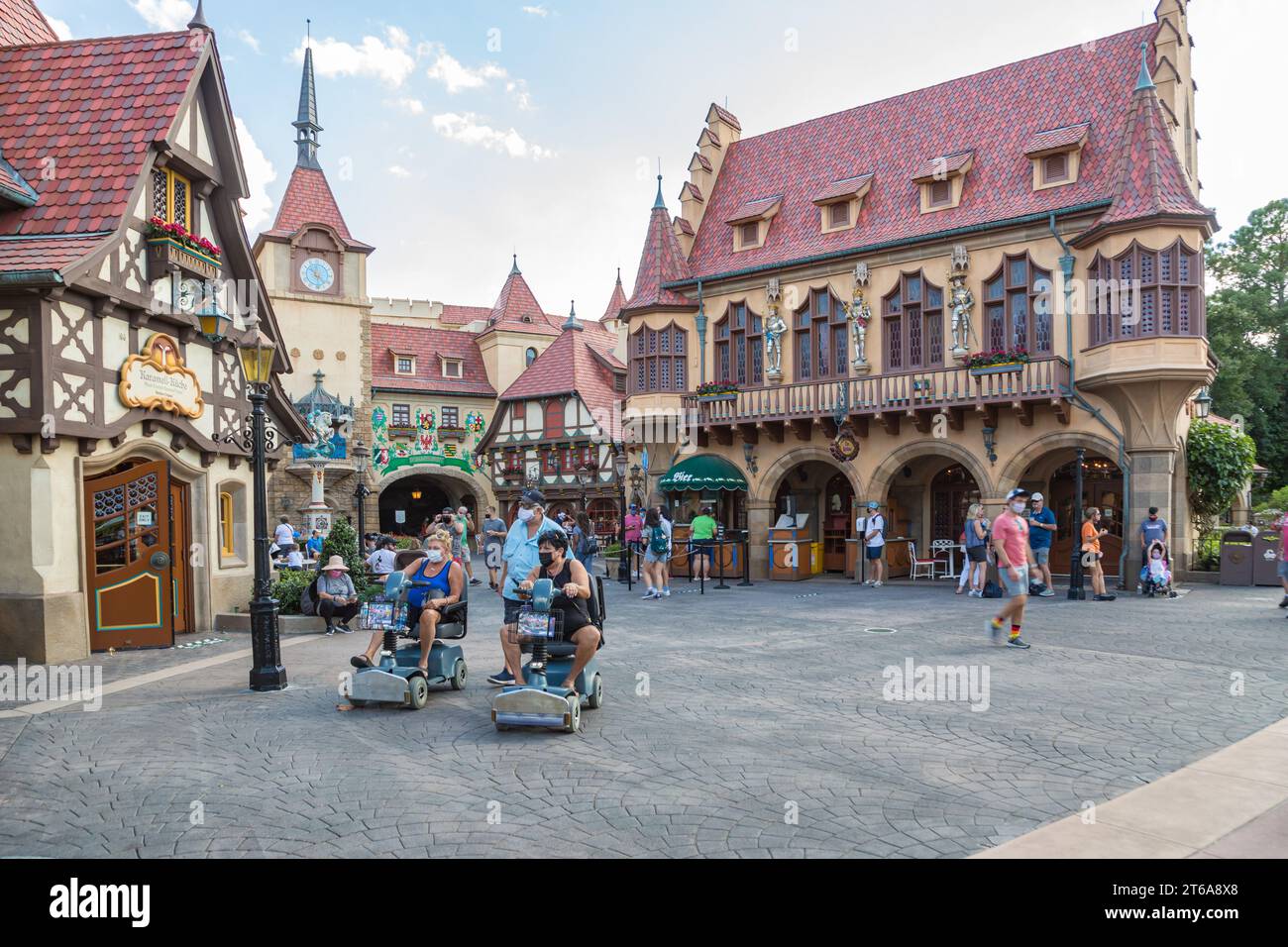 Les clients du parc masqué marchent et font du scooter à travers le pavillon allemand d'Epcot au Walt Disney World à Orlando, en Floride Banque D'Images