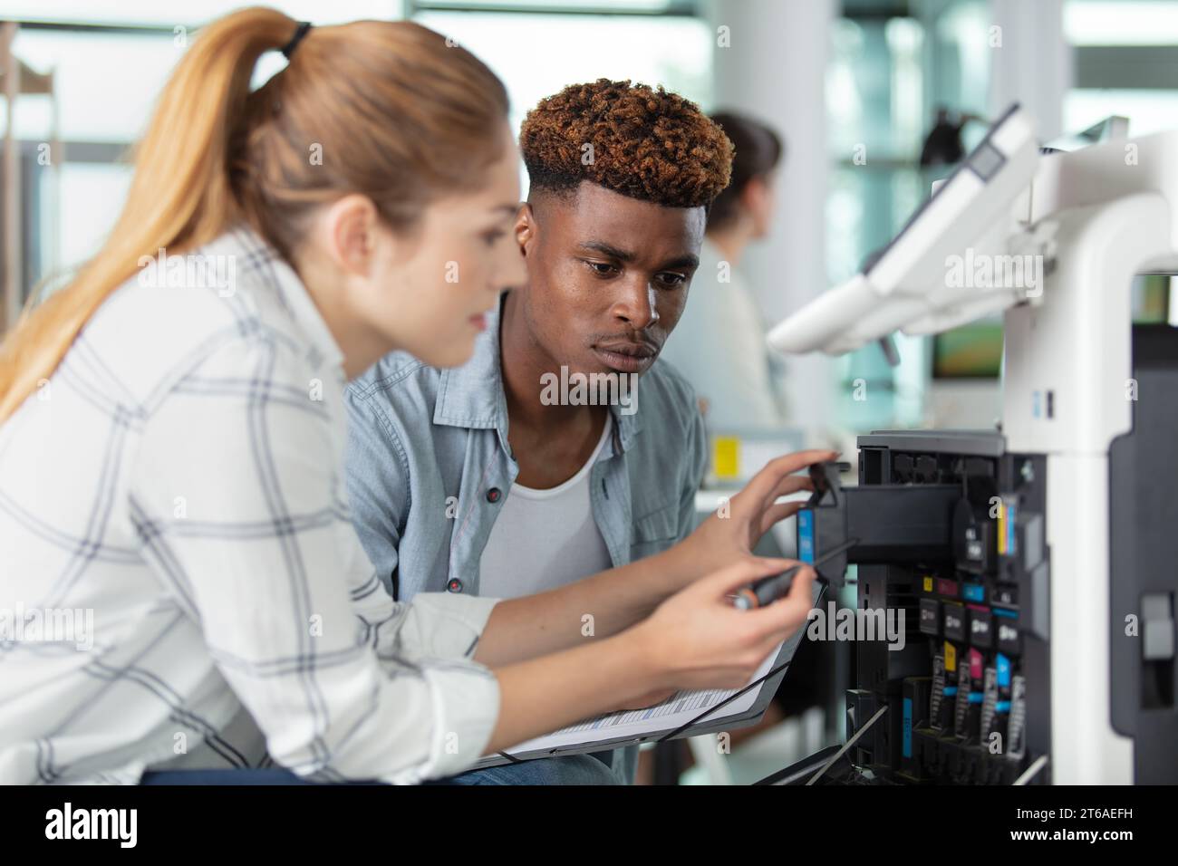 homme regardant la femme remplacer la cartouche d'encre dans l'imprimante industrielle Banque D'Images