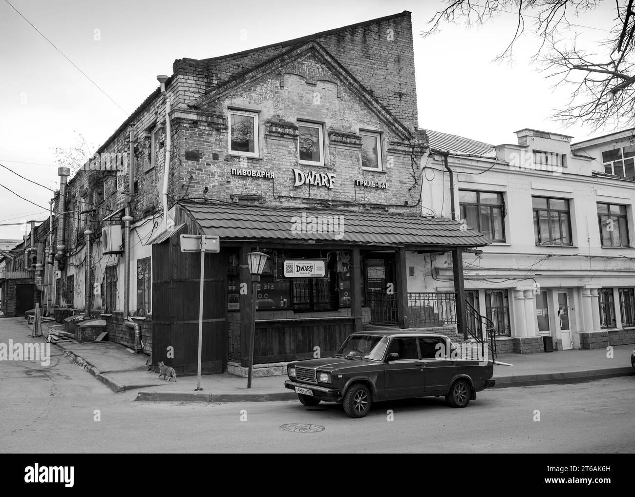 Une rue avec une brasserie dans une vieille maison en briques, une voiture rétro et un chat. Inscription : 'Brasserie, Grill bar' Banque D'Images
