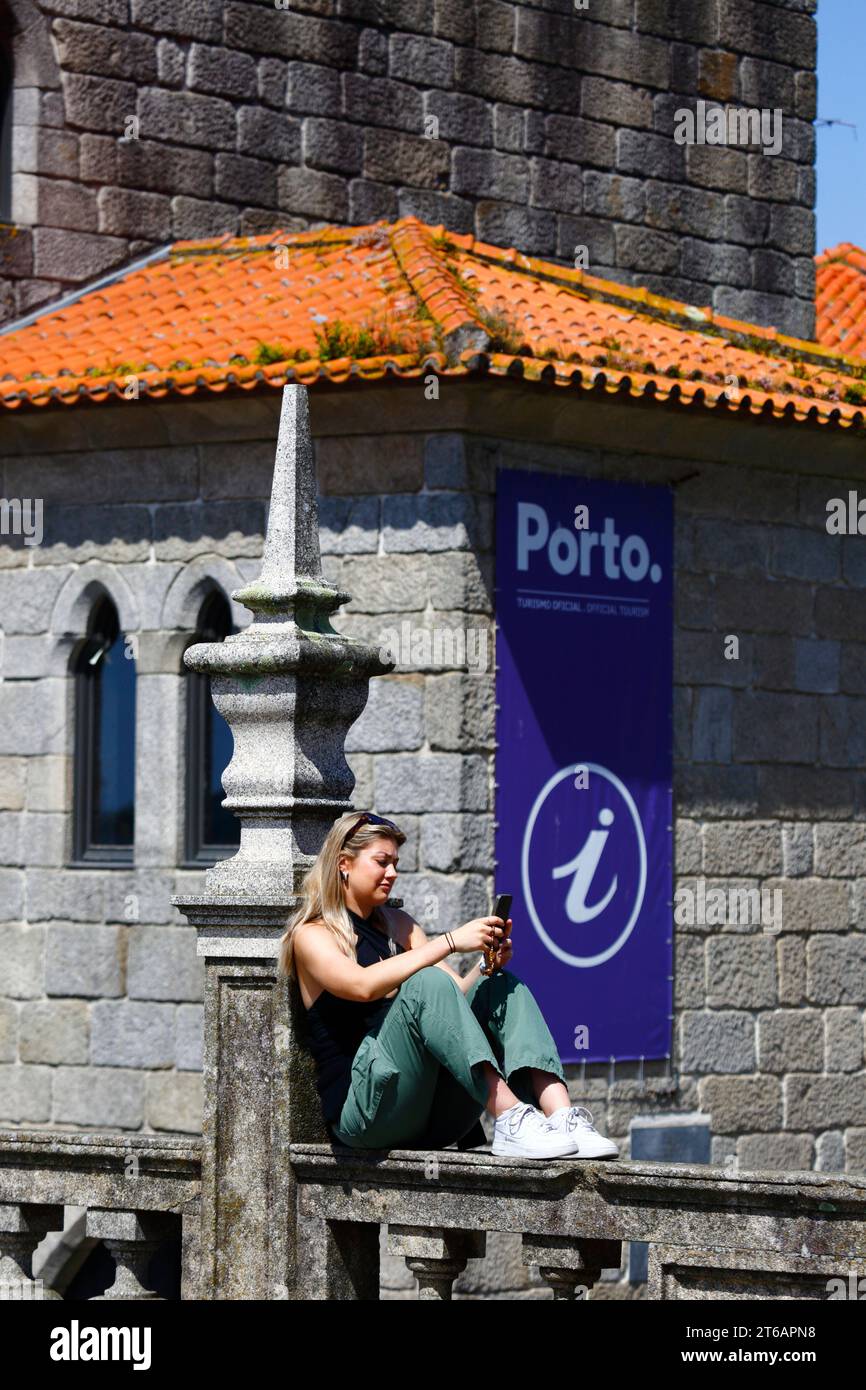 Une touriste regarde son smartphone devant le bureau de l’Association touristique de Porto, terrasse Terreiro da Sé, Porto / Porto, Portugal Banque D'Images