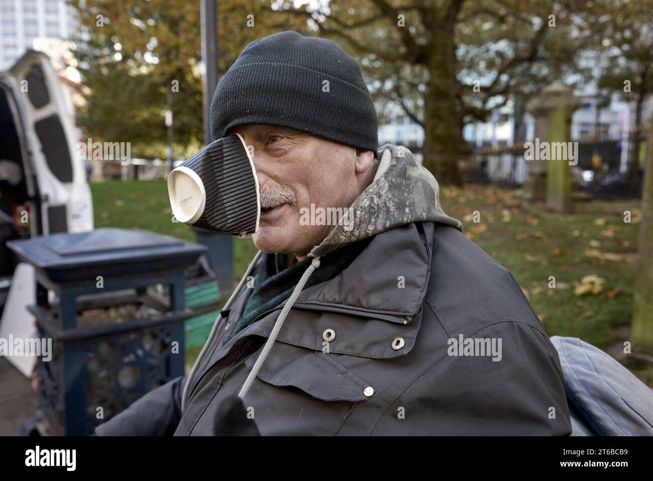 Improvisation. Homme âgé avec une tasse à café usagée protégeant son nez de l'air froid de l'hiver. Banque D'Images