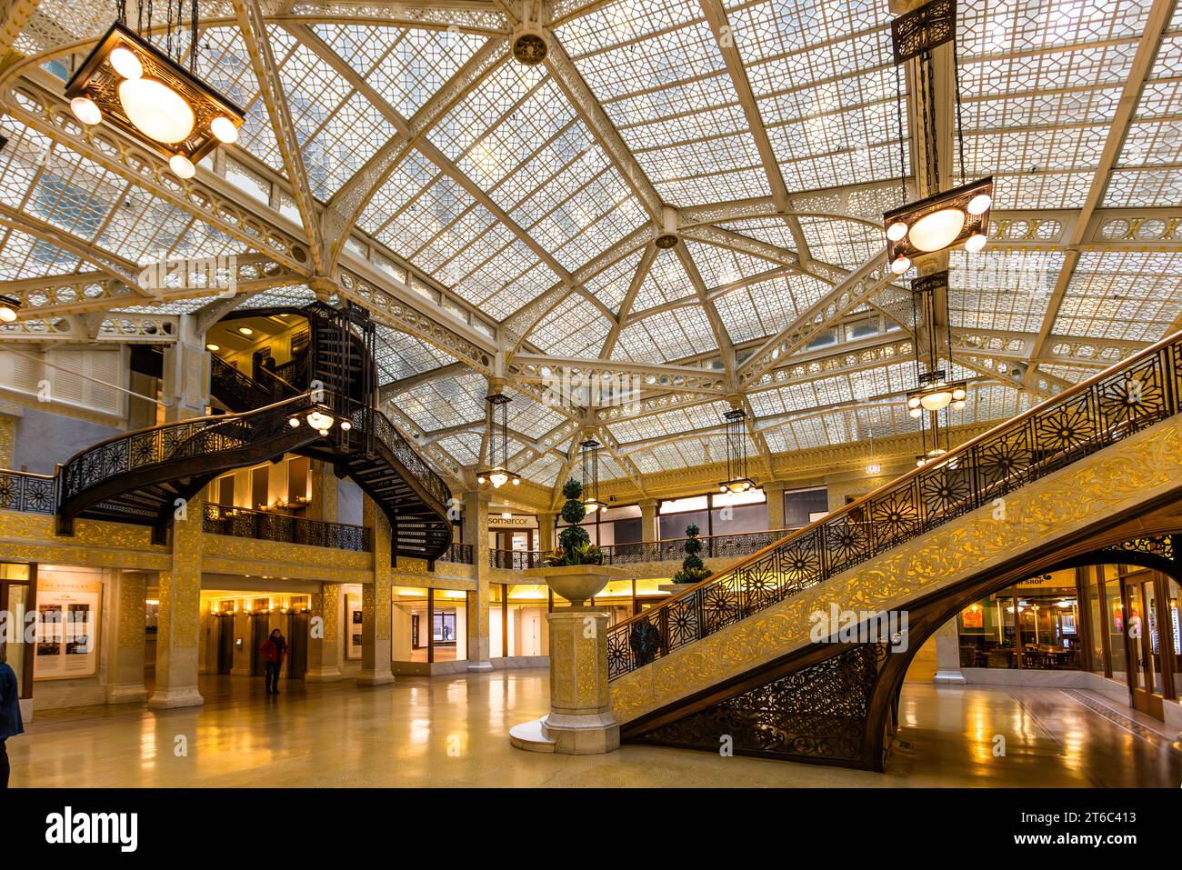 Le sol en marbre clair et l'escalier courbé doré marquent la cour lumineuse du Rookery Building à Chicago, Illinois, États-Unis. De petits arbres en pot et des vitrines bordent la galerie du rez-de-chaussée, et le bâtiment est encore utilisé aujourd'hui comme immeuble de bureaux. Banque D'Images