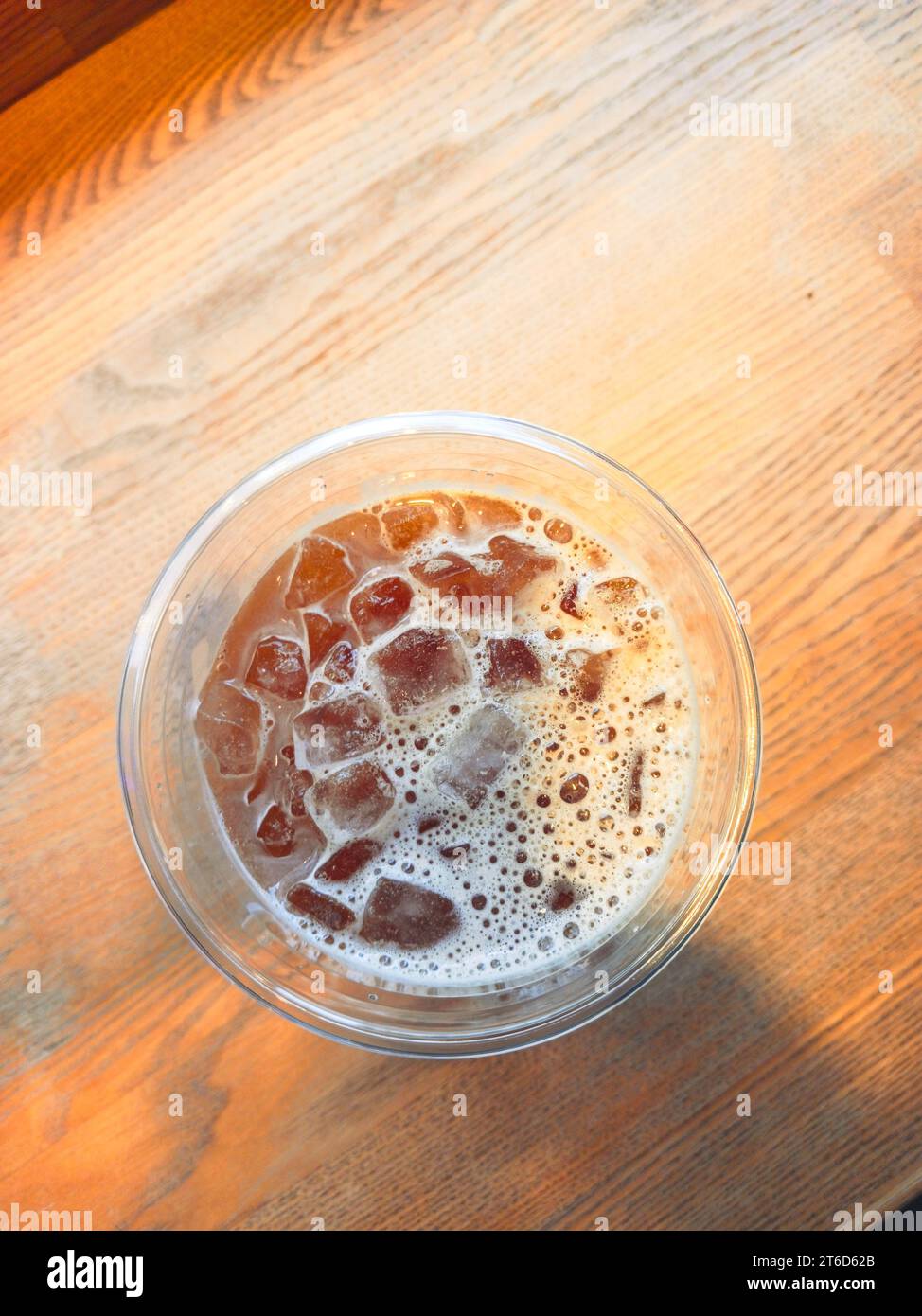 Une tasse d'Americano glacé avec des glaçons placé sur une table en bois dans un café. Vue de dessus d'un verre de café à la lumière du soleil du matin Banque D'Images