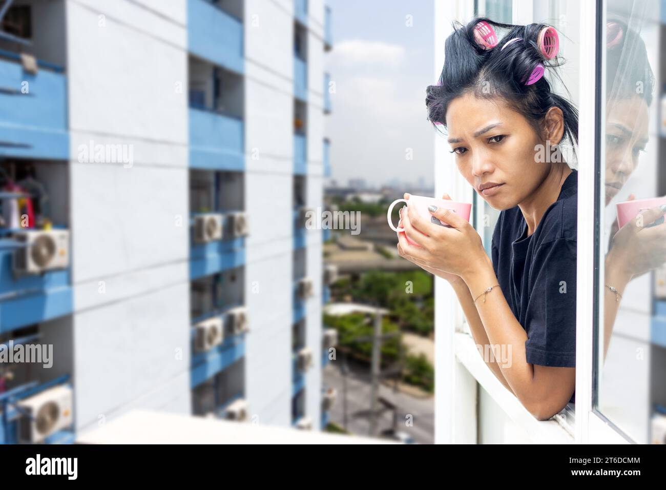 Une jeune femme en curleurs regarde par la fenêtre d'un immeuble de grande hauteur Banque D'Images