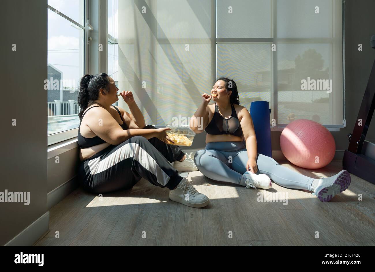 Deux femmes de grande taille appréciant joyeusement leur repas, assis dans une salle de fitness, favorisant la positivité corporelle et la vie joyeuse. Banque D'Images