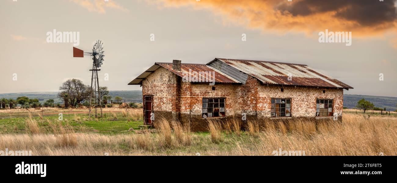 ancienne maison de ferme en ruine avec un moulin à vent vintage haute herbe sèche au premier plan Banque D'Images