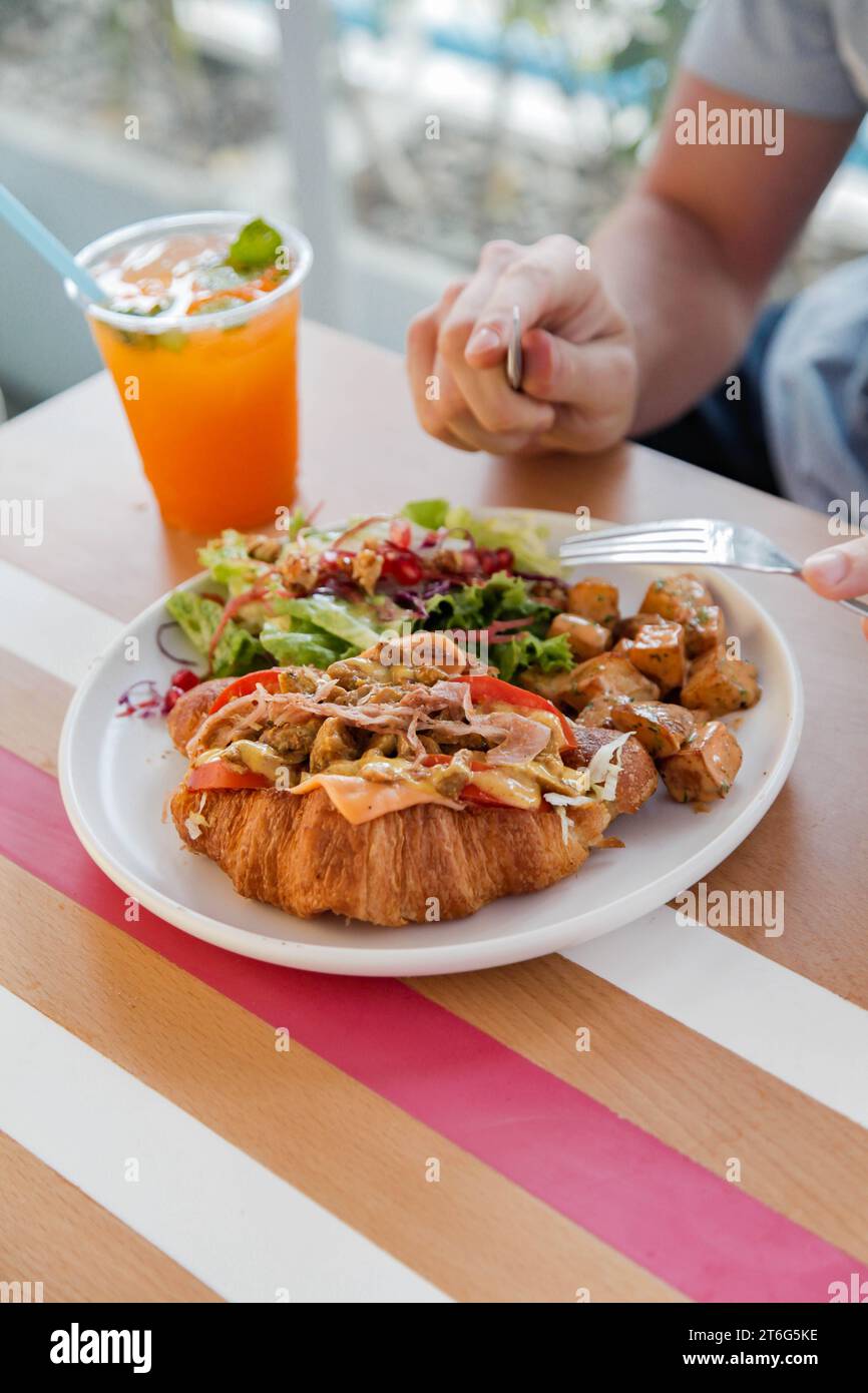 Personne ayant un sandwich au poulet croissant ouvert face avec des légumes sur le côté. Banque D'Images