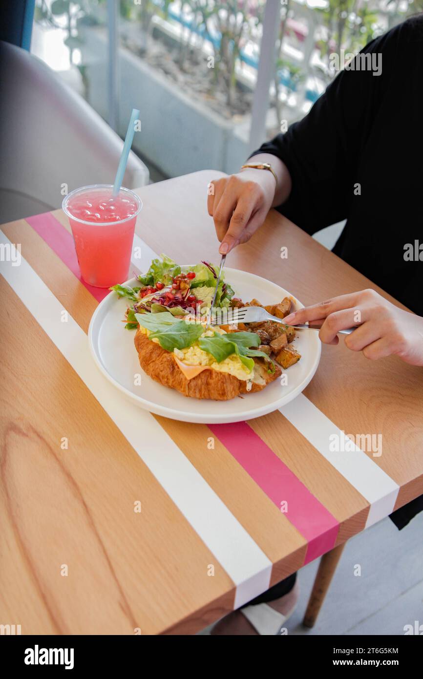 Personne ayant un sandwich au poulet croissant ouvert face avec des légumes sur le côté. Banque D'Images