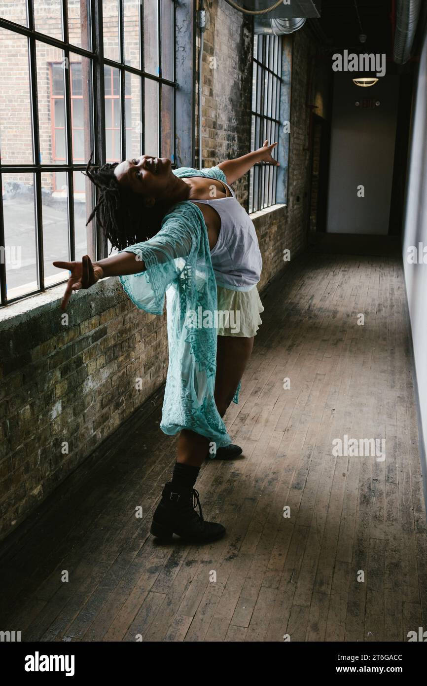 Danseur pose dans le couloir éclairé par la fenêtre avec une veste sarcelle et des bottes Banque D'Images