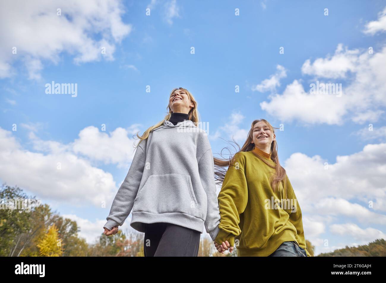 deux jeunes filles joyeuses courant main dans la main contre le ciel Banque D'Images