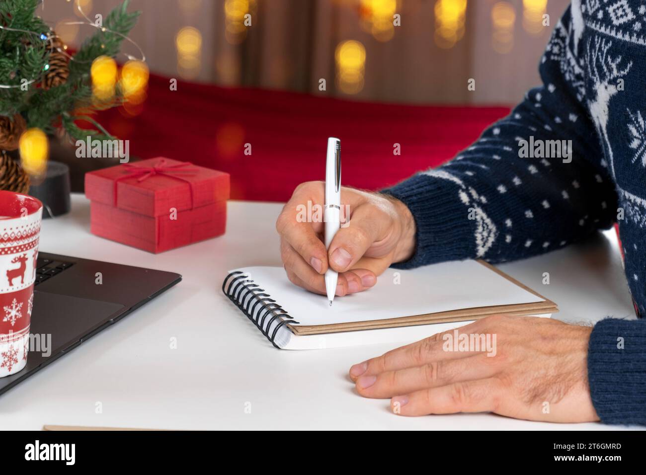 Ecriture d'une carte de vœux de Noël. Homme adulte faisant des cartes de voeux au bureau à domicile pendant Noël. Les mains de l'homme dans le chandail bleu tenant le papier vierge et envel Banque D'Images