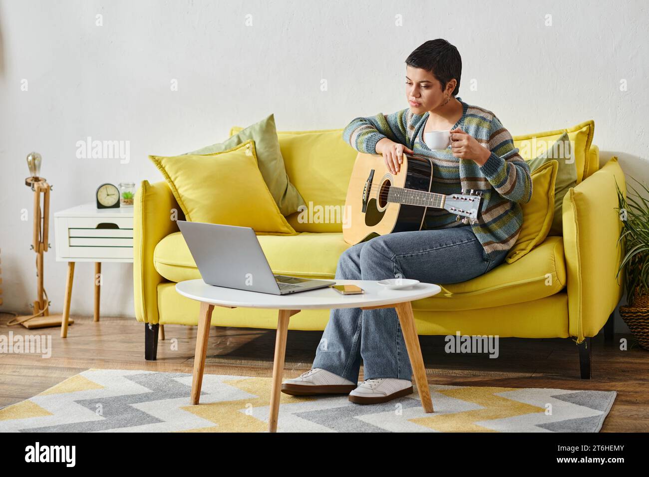 concentré jeune femme assise sur un canapé avec guitare pendant la leçon de musique en ligne, l'éducation à la maison Banque D'Images