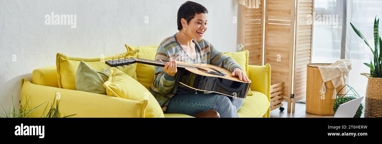 heureuse femme aux cheveux courts tenant la guitare pendant la leçon de musique à distance, éducation à la maison, bannière Banque D'Images