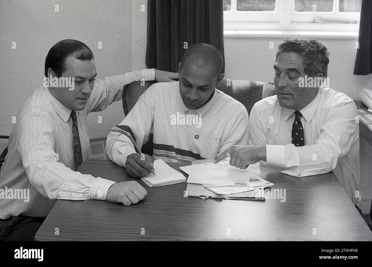 1989, opération Raleigh, assis à une table avec deux hommes du personnel, un jeune homme prenant des notes avant son travail de bénévole pour l'organisme de bienfaisance, Angleterre, Royaume-Uni. Inspirée par une expédition de voile, Operation Drake, Operation Raleigh a été fondée en 1984 en tant qu’organisation bénévole de jeunes pour aider ceux qui vivent dans des zones rurales reculées et, à leur tour, permettre aux jeunes de voyager, de développer leur caractère et d’aider ceux qui ont moins de ressources. Banque D'Images