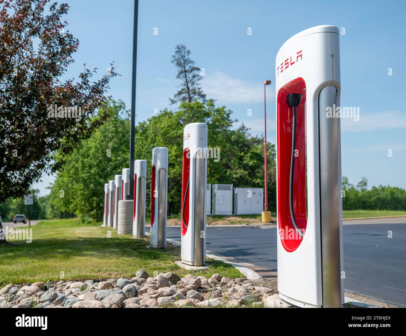 BEMIDJI, MN – 3 JUIN 2023 : une rangée de stations de recharge Tesla Supercharger près de l'herbe verte et des arbres et un ciel bleu dans le Minnesota. Banque D'Images