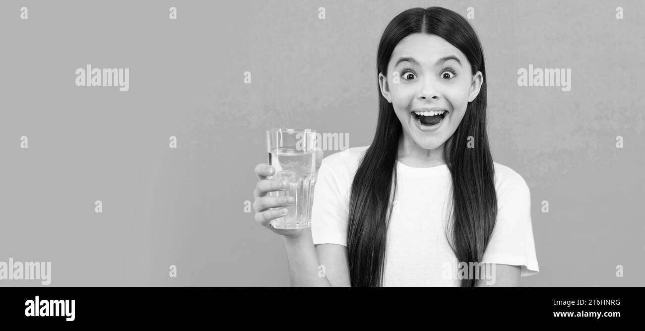 une fille surprise boit un verre d'eau pour rester hydraté et garder l'équilibre quotidien de l'eau, boire de l'eau. Bannière d'enfant fille avec verre d'eau, studio Banque D'Images