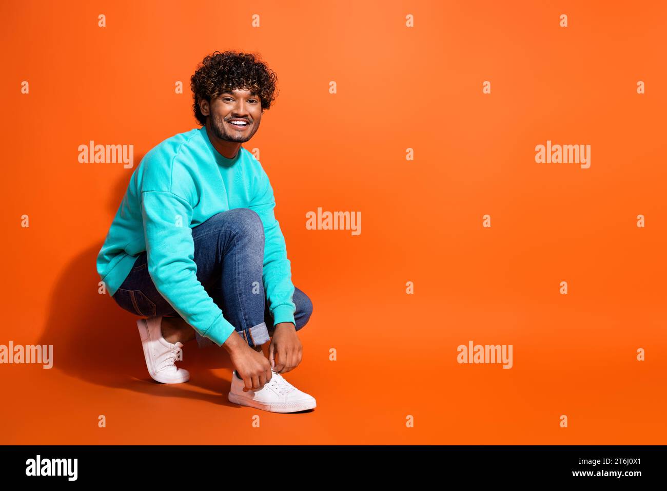 Photo de pleine longueur de mec indien joyeux annonçant de nouvelles baskets marque adidas laçage vers le haut du plancher assis isolé sur fond de couleur orange Banque D'Images