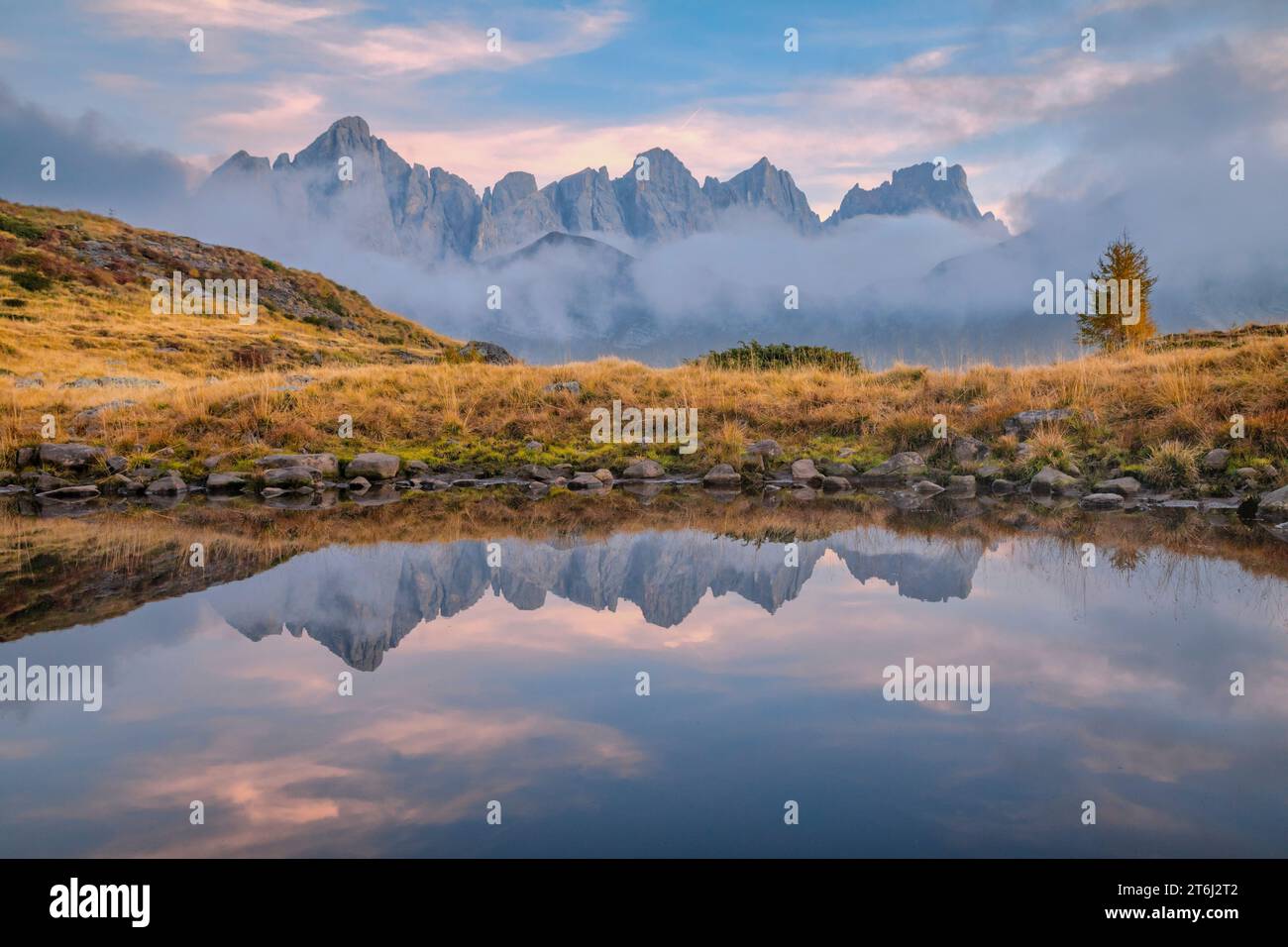 Italie, Vénétie, quartier de Belluno, Falcade, coucher de soleil brumeux en automne avec le côté nord de la Pale di San Martino reflété sur un étang alpin, Dolomites Banque D'Images