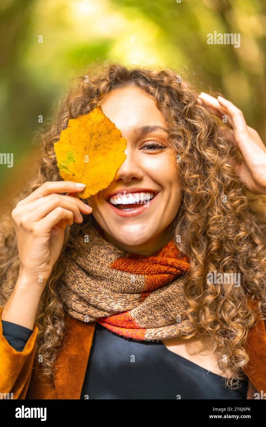 Portrait d'automne vertical d'une femme souriante avec les cheveux bouclés se cachant sur une feuille Banque D'Images