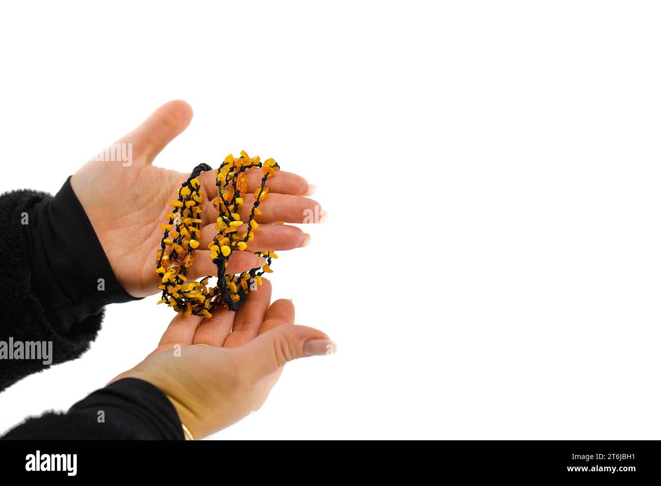 L'image représente un collier en ambre poli sur un cordon noir, délicatement tenu dans des mains féminines. Les teintes dorées contrastent avec le noir. Banque D'Images