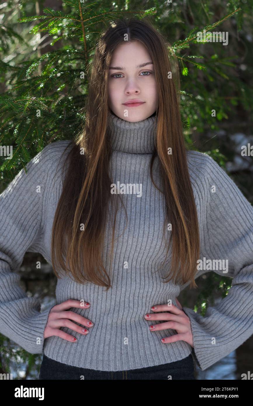 Portrait d'une adolescente confiante armes akimbo et regardant la caméra. Brunette adolescent portant en chandail gris debout dans la forêt de pins. Vue avant Banque D'Images