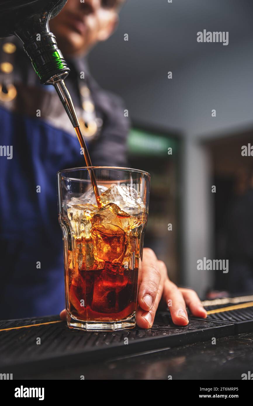 Barman versant l'alcool de bouteille dans le verre sur le comptoir-bar pour préparer la boisson alcoolisée mélangée à servir dans la fête de boîte de nuit. Banque D'Images