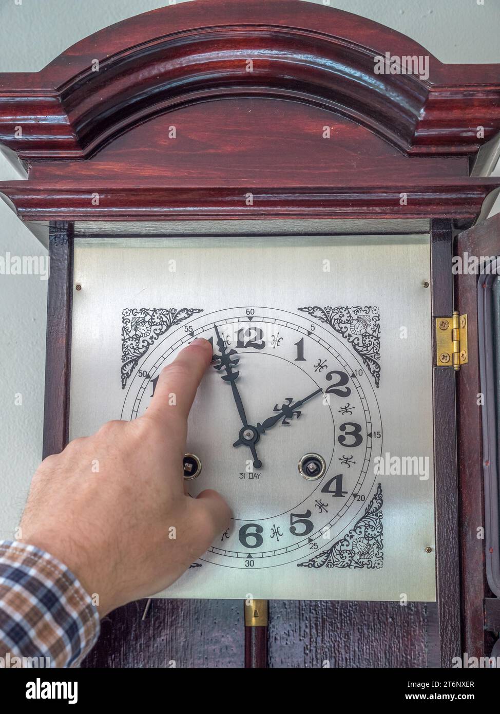 Gros plan du doigt masculin changeant les aiguilles de l'horloge de l'heure d'été à l'heure d'hiver Banque D'Images