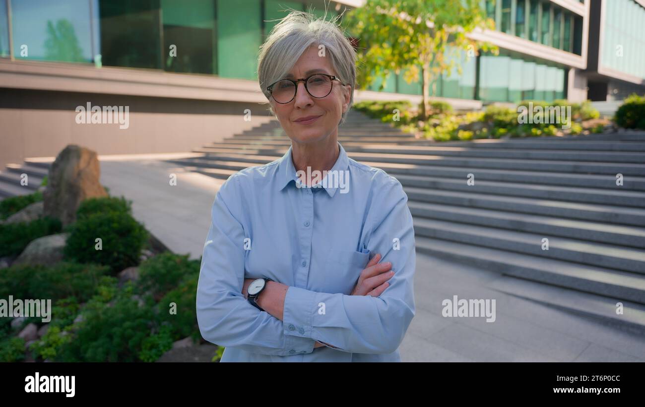 Portrait réussi de femme d'affaires caucasienne d'âge moyen à l'extérieur souriant vieux senior mature 50s employeur d'affaires femme aux cheveux gris avec les mains croisées Banque D'Images