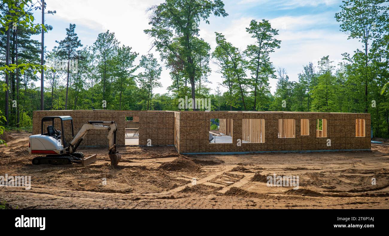 Nouveau projet de construction de maison sur un terrain à bâtir boisé, avec une mini pelle stationnée sur la terre au chantier de construction. Banque D'Images
