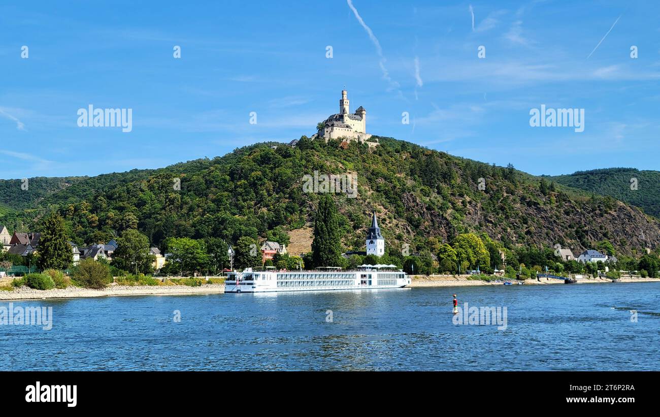 Château de Marksburg au-dessus du Rhin dans la ville de Braubach en Rhénanie-Palatinat, Allemagne, avec un long bateau de croisière fluvial amarré en dessous. Banque D'Images