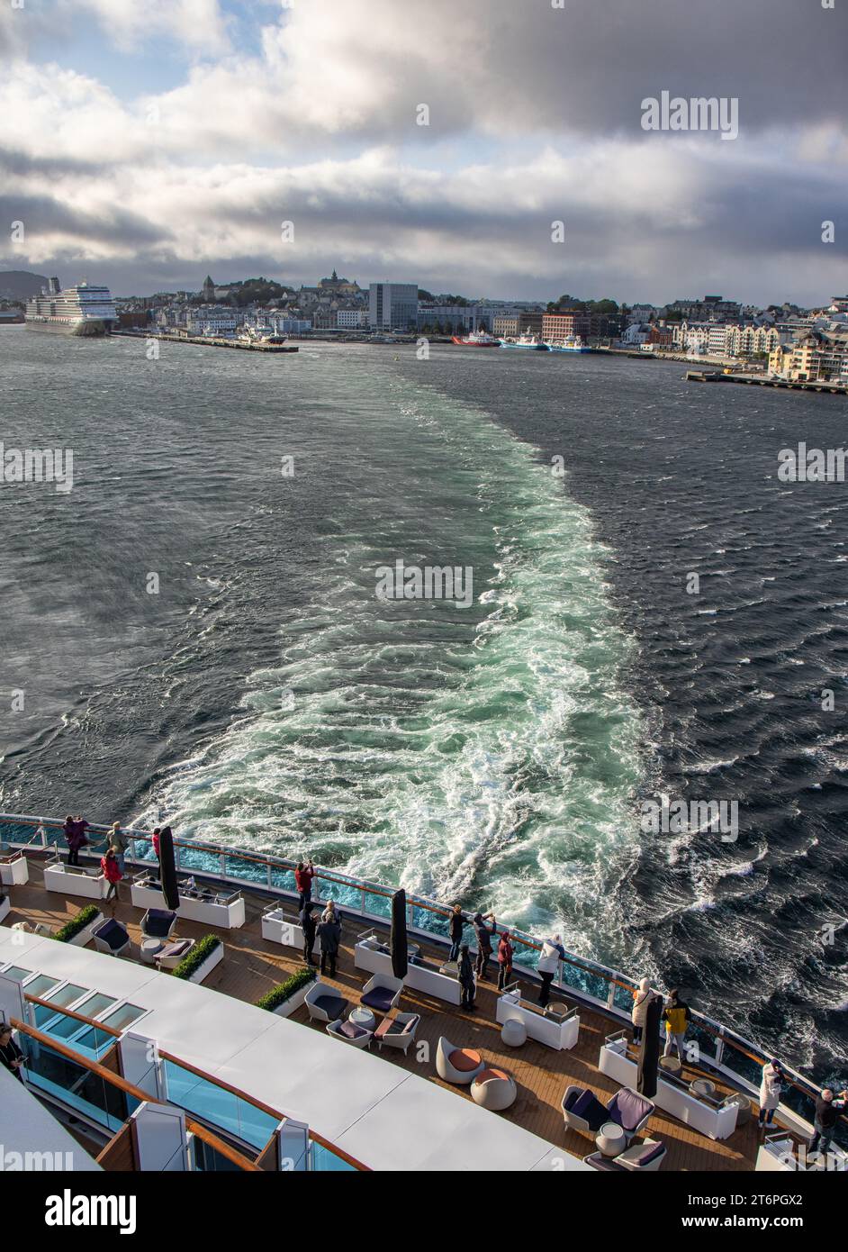 La Ciudad de Alesund desde la salida de un crucero, estela de barco y cielo tormentoso. Turistas en la cubierta del barco tomando fotografías. Noruega Banque D'Images
