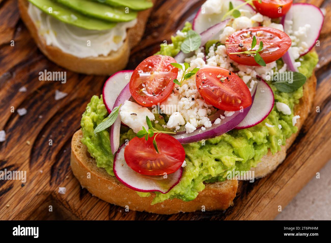 Toasts d'avocat avec radis, tomates et feta garnis d'huile d'olive, idée de petit déjeuner sain Banque D'Images