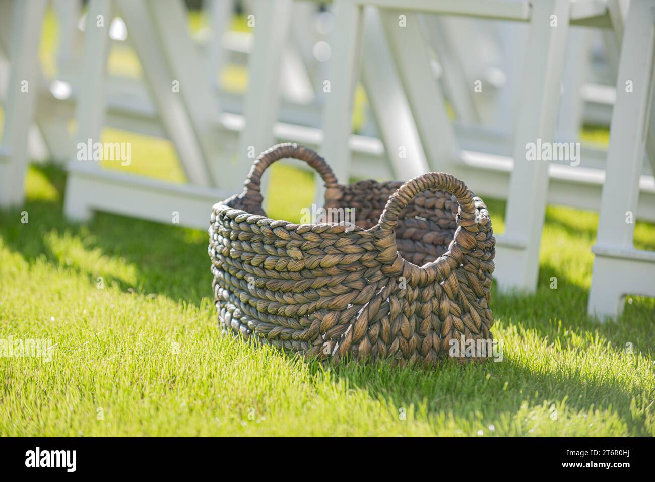 Panier en osier brun vide avec poignées rondes sur l'herbe devant des chaises blanches à la cérémonie de mariage isle Banque D'Images