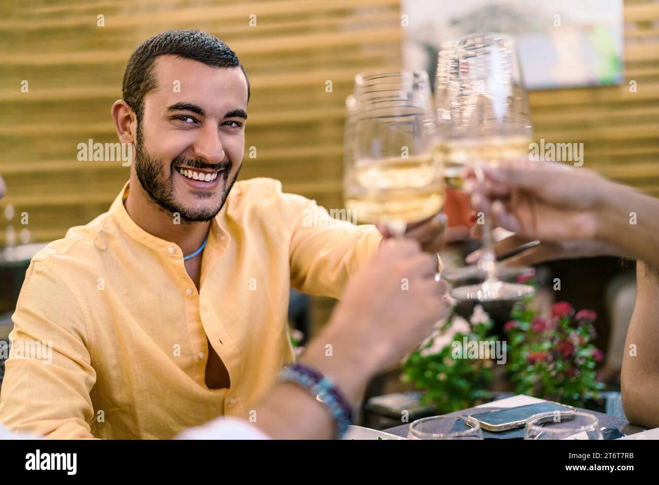 Un homme souriant dans une chemise jaune grillant avec du vin blanc, profitant d'un moment convivial avec des amis - agréable dégustation de vin, toast amical avec Banque D'Images