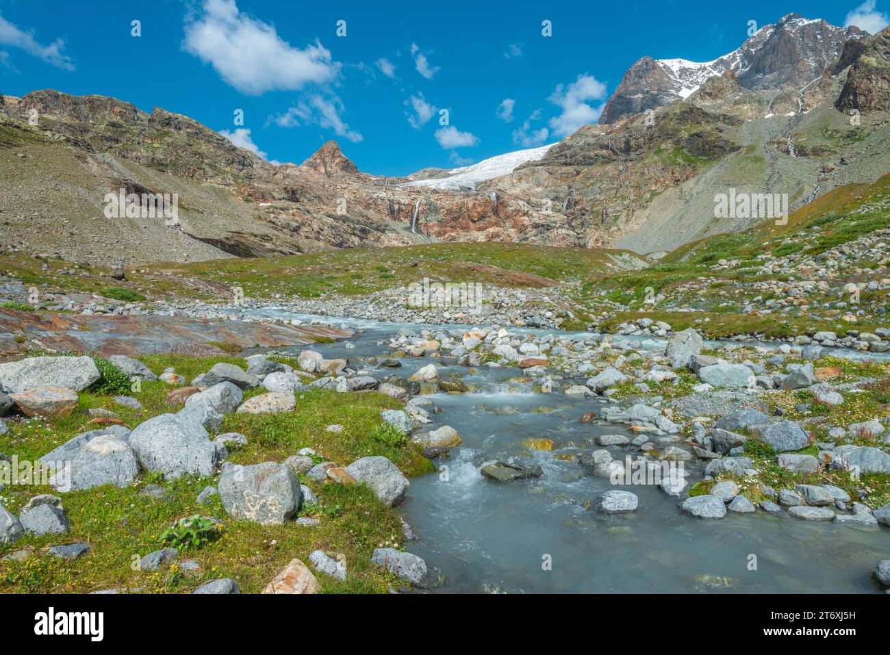 Vallée de montagne luxuriante en été, ruisseau glaciaire se précipitant à travers le fond de la vallée. Roches et rochers et herbe verte fraîche. Banque D'Images