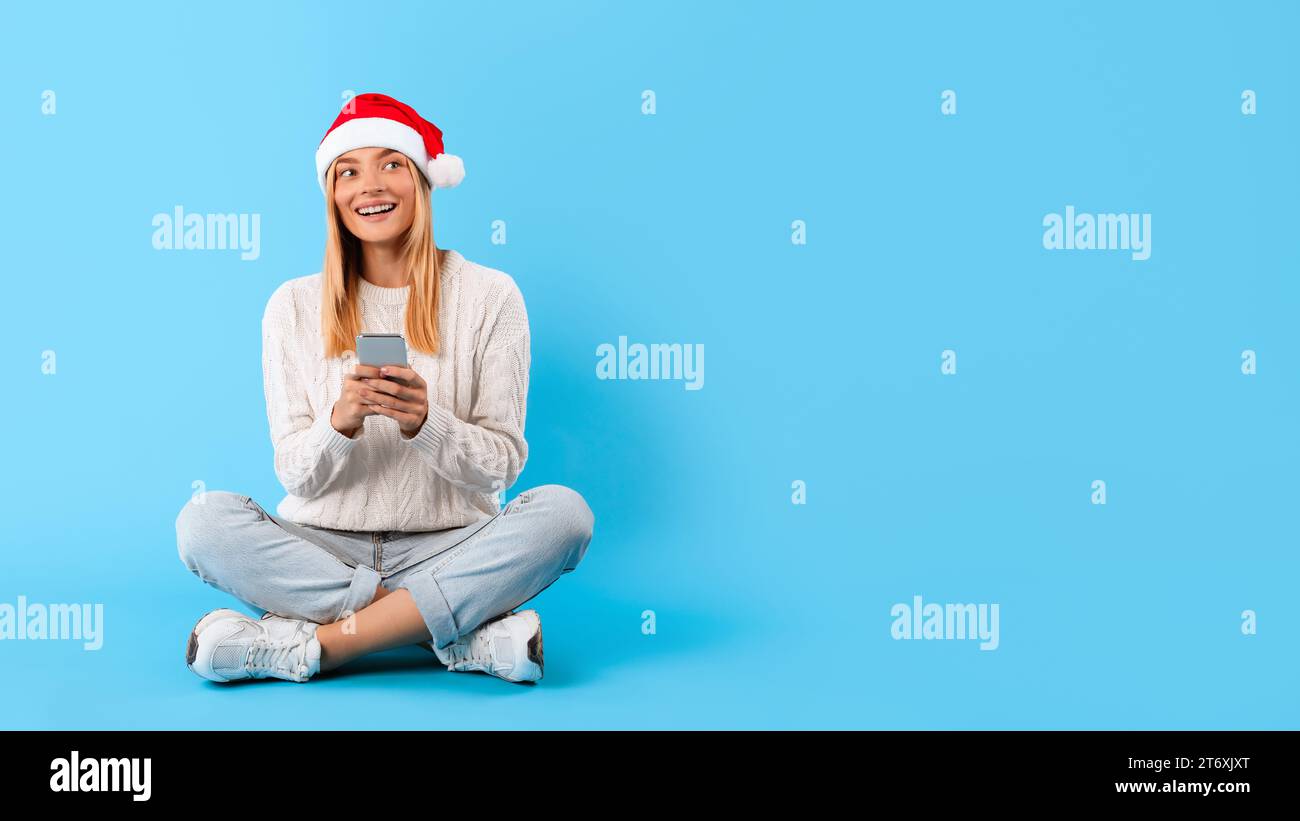 Femme heureuse dans le chapeau de Santa en utilisant le téléphone et en regardant l'espace libre Banque D'Images