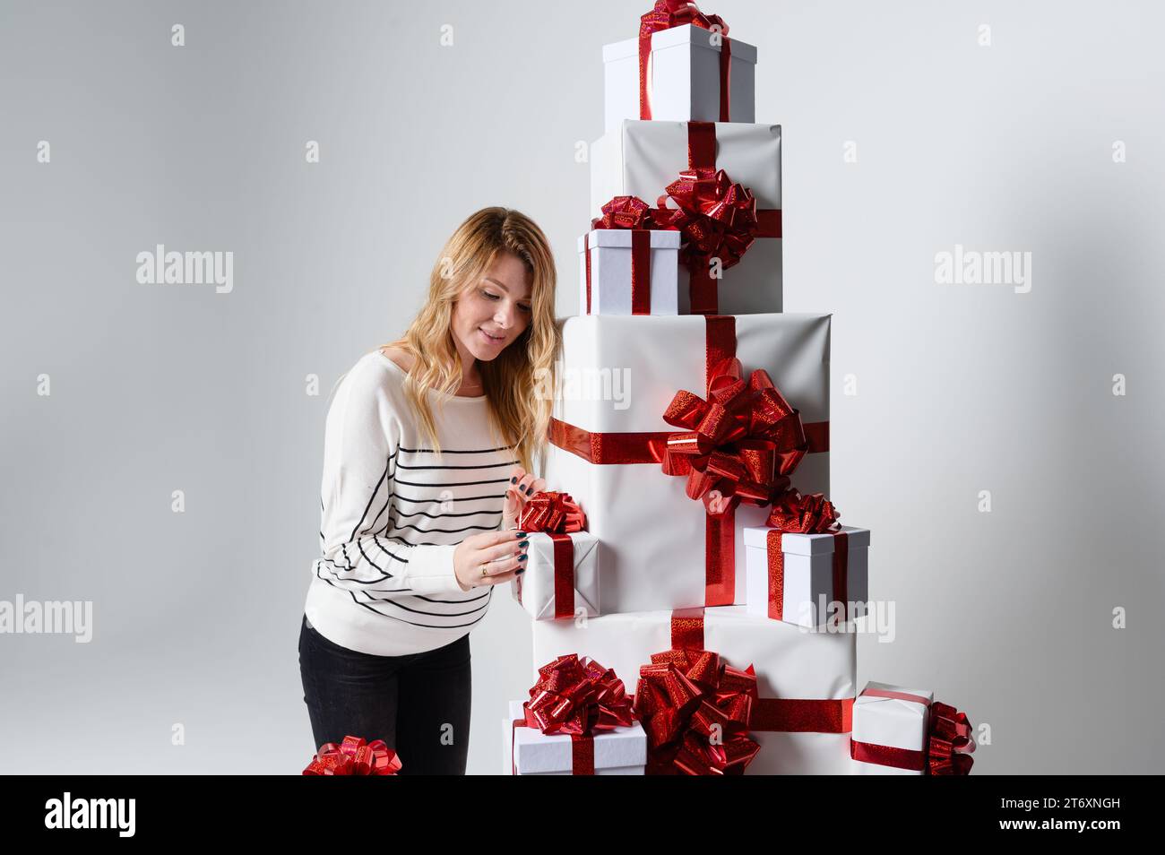 Une belle jeune femme magnifique pose parmi une montagne de boîtes-cadeaux blanches dans un fond gris. Joliment décoré pour Noël. Mode vacances Banque D'Images