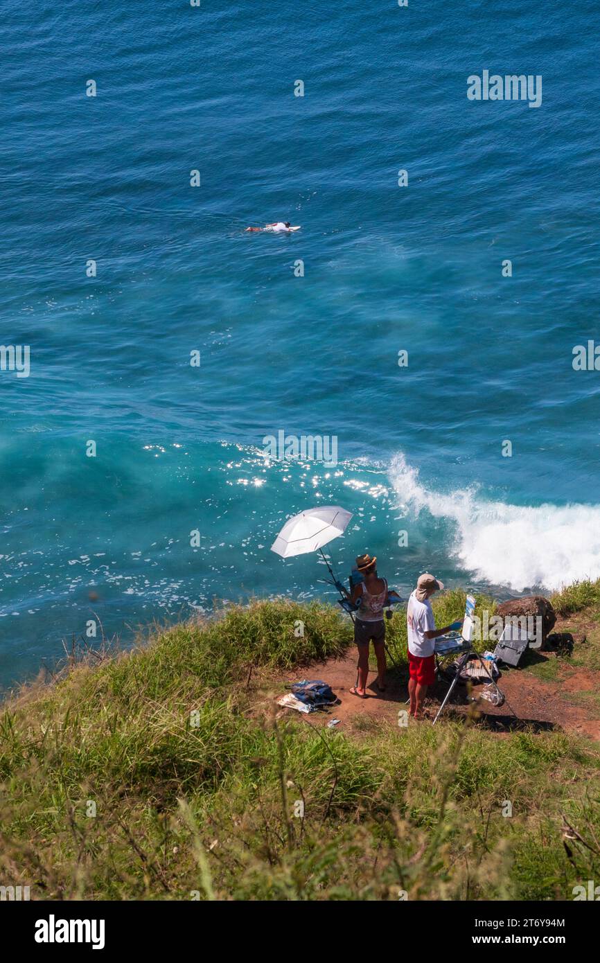 Deux personnes en plein air peinture sur une falaise surplombant l'eau tropicale bleu turquoise avec un surfeur pagayant sur Maui, Hawaï, États-Unis. Banque D'Images