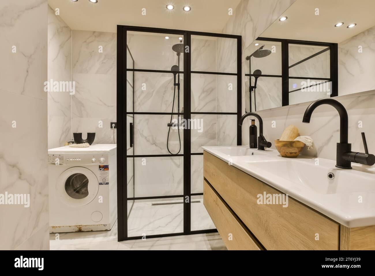 une salle de bains moderne avec des murs en marbre blanc et des miroirs encadrés noirs sur le mur, il y a une rondelle dans le coin Banque D'Images
