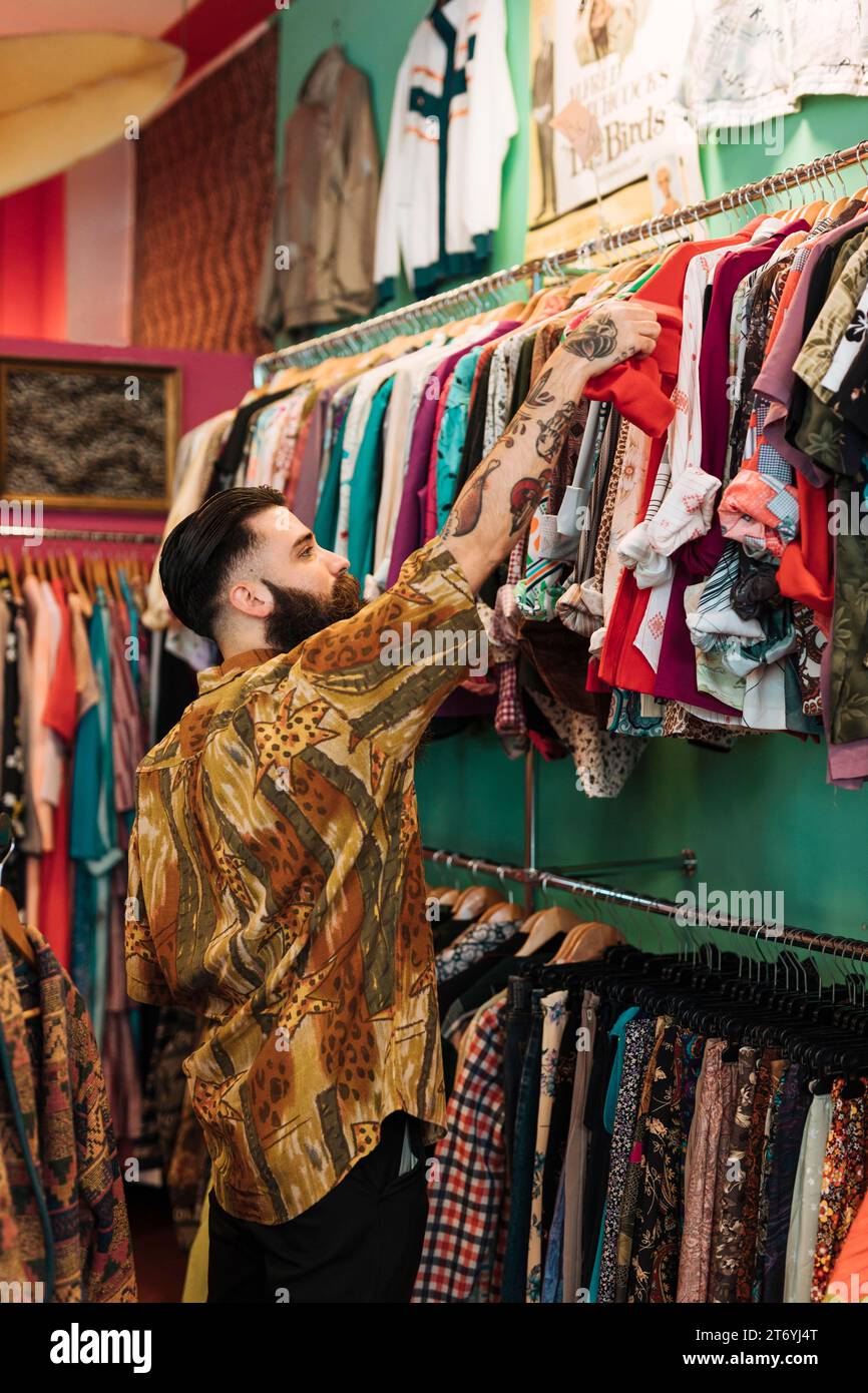 Jeune homme barbu choisissant un t-shirt rouge de la boutique de vêtements de rail Banque D'Images