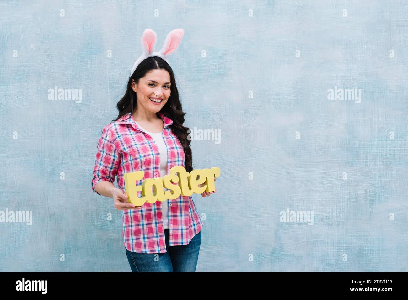 Femme souriante avec l'oreille de lapin montrant le mot de pâques sur fond bleu texturé Banque D'Images