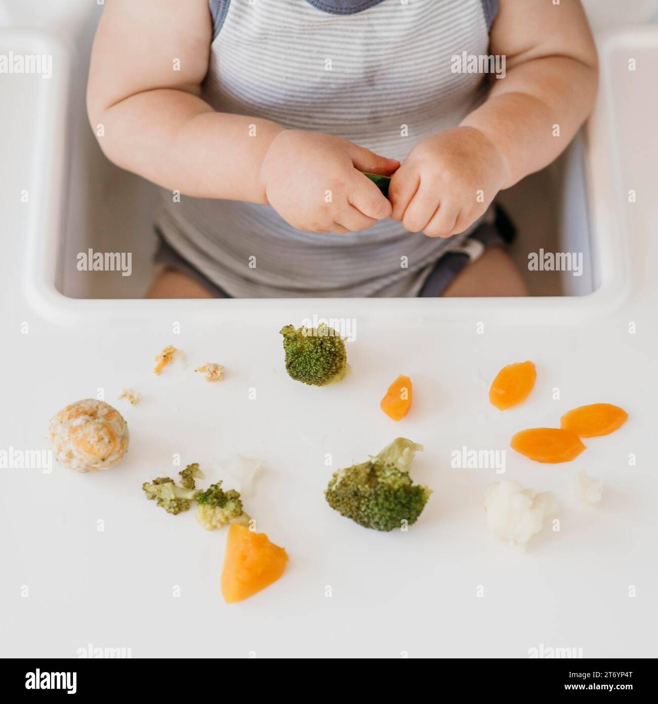 Chaise haute bébé garçon mangeant des légumes seul Banque D'Images