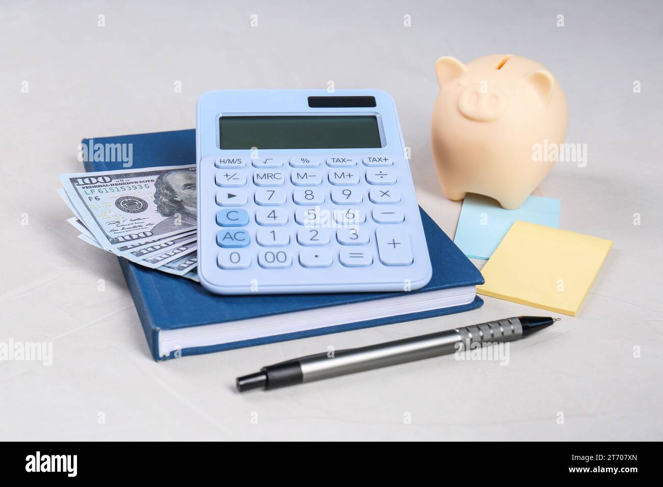 Calculatrice, billets de banque en dollars, tirelire, cahier, notes autocollantes et stylo sur la table gris clair. Concept de retraite Banque D'Images