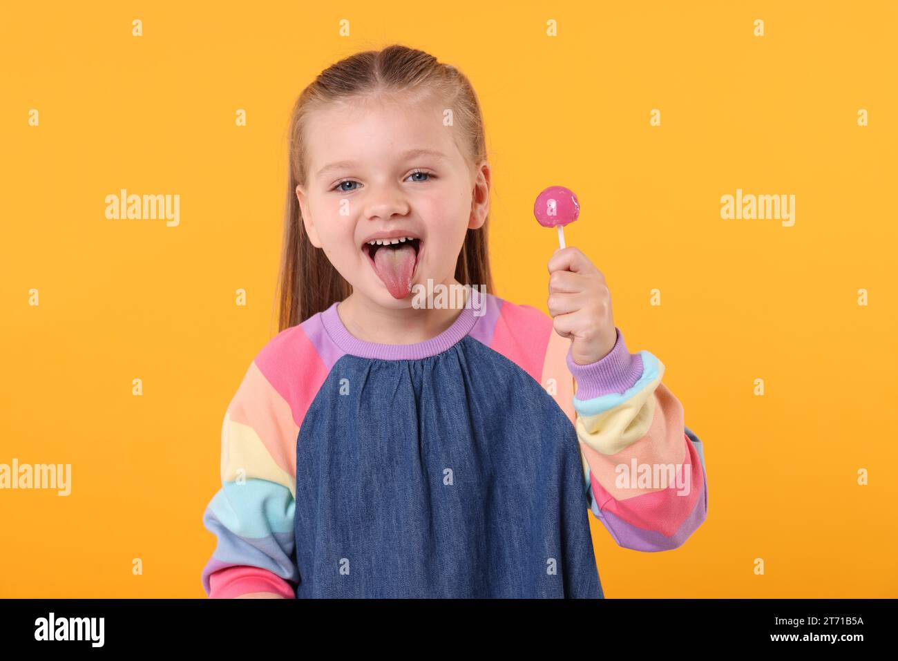 Petite fille avec sucette montrant la langue sur fond orange Banque D'Images