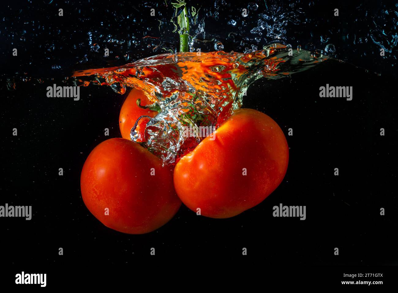 Tomate rouge fraîche tombant dans l'eau avec des éclaboussures d'eau et des bulles d'air isolées sur fond noir. Banque D'Images