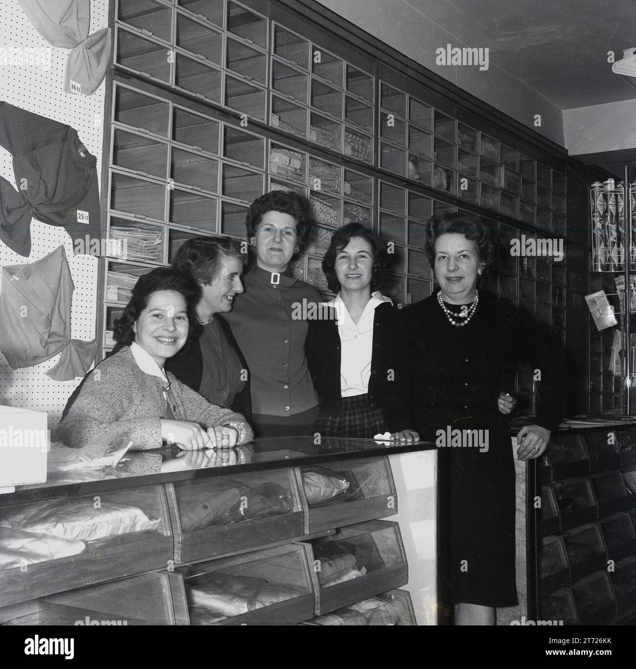 Dans les années 1960, des assistantes de magasin, gérante et propriétaire historiques se sont réunies pour une photo à l'intérieur d'un magasin vendant des hauts, des pulls et des cardigans en laine pour femmes, Angleterre, Royaume-Uni. Présentoirs traditionnels en bois pour les vêtements sur le mur derrière. Banque D'Images