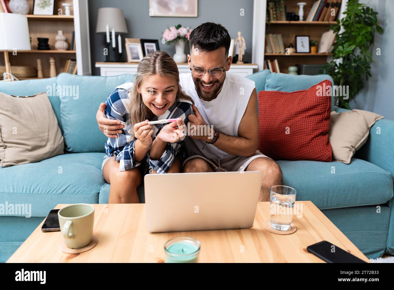 Couple heureux surpris annonçant leur grossesse à la famille et aux amis lors d'un appel vidéo. Jeunes futurs parents utilisant un ordinateur portable pour partager leur Banque D'Images